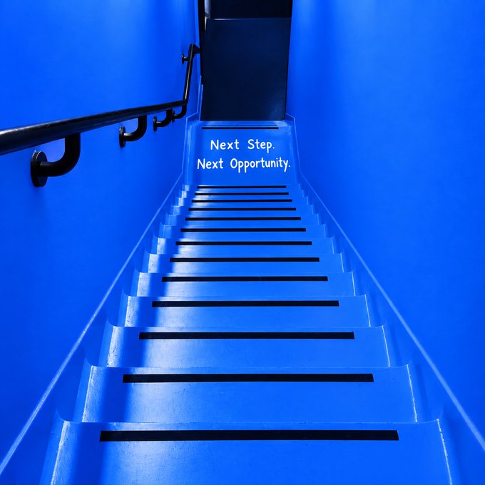 A vibrant blue staircase ascends toward a doorway, with the words "Next Step. Next Opportunity." projected at the top, symbolizing upward progression and new beginnings. The image visually echoes the prompt's message about taking decisive action—"GM" (good morning) and "What's your next move?"—by encouraging viewers to climb toward opportunity.