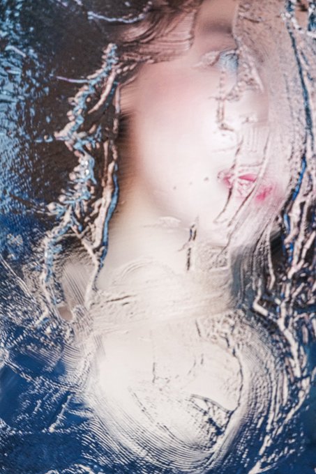 Distorted, abstract portrait with swirling blue and white patterns obscuring a face, with visible pale skin and pink lips in the center.