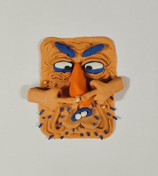 A clay sculpture of a face with wild orange hair, angry blue eyebrows, a long pointed nose, and a wide mouth with blue spike-like details.