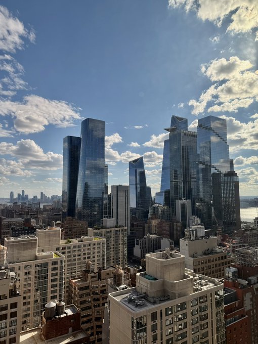 The image shows a city skyline with tall buildings, including skyscrapers that have reflective windows. The sky above the city appears cloudy, creating an interesting contrast between the urban landscape and the natural elements. In the foreground of the photo, there is text that reads "One of our engineers and myself are at ethconf this week. Hmu if you'r around!". This suggests that a group of people might be attending or participating in an event related to ethical computing.