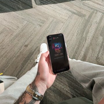 Holding up a phone that shows a "TOTAL WIN" of "$987.00" from a game, likely on a casino app, as they're at an airport. The "GO BRRRRR" in the post suggests rapid winning or excitement about the win.