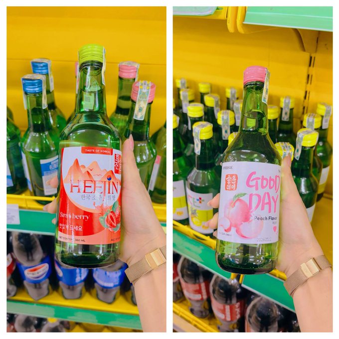 The image shows two bottles of alcohol, one green and one pink, being held by a person's hand. The person is standing next to a shelf filled with various types of alcohol bottles. The background of the image features a yellow wall that has the words "hôm nay k có chút tâm trạng lướt x luôn đó trời." and "nhà nhà được payx người giờ mở vô thì chút tâm trạng lướt x luôn đó trời." The image is a collage of two photos, with the person holding one bottle and the shelf filled with bottles in the background.