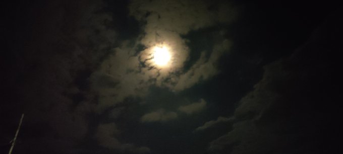 A nighttime photograph of a bright full moon partially obscured by wispy clouds in a dark sky.