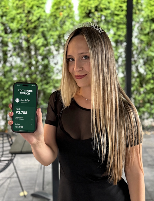 Young woman with blonde hair wearing a birthday tiara and black sheer top, holding a smartphone displaying a 'Common Vouch' app screen showing @ooSofya with 2,788 verified subscribers.