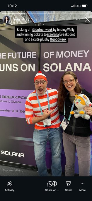 The image shows a man wearing an orange and white striped shirt holding a stuffed animal while standing next to a woman who is also holding a stuffed animal, both of them smiling for the camera. The background features a poster with text about Solana Breakpoint tickets being sold at a special event in November 15-17.