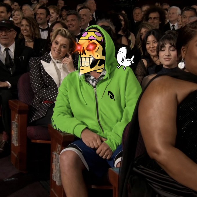 A person in a bright green hoodie with a skull mask sits in an audience, with a small cartoon bird perched on their shoulder, surrounded by formally dressed attendees.