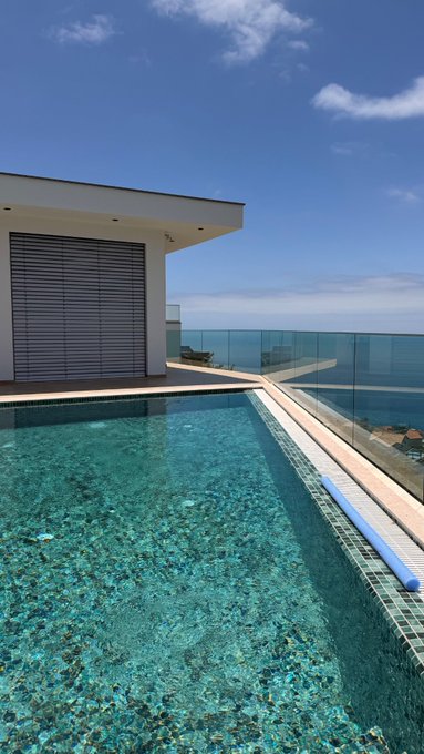A serene infinity pool overlooking the ocean under a clear blue sky, paired with a modern minimalist building. The luxurious coastal view evokes the "good morning" vibe of the post, inviting viewers to share their $SOL address in a setting that mirrors the high-value, aspirational lifestyle often associated with crypto enthusiasts.