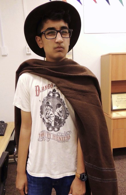 A young man wearing a black wide-brimmed hat, glasses, and a brown poncho over a "Django Unchained" graphic t-shirt stands in what appears to be a classroom or office setting, with a laptop and wooden cabinet visible in the background.

The image connects to the post by likely depicting a meme/degens trader wearing the signature Django Unchained poncho (a popular crypto degen aesthetic), humorously personifying the $40M losses suffered by top FOMO traders following FrankDeGods' $2.4M memecoin exit.