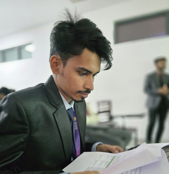 A focused young man in a dark suit and purple tie intently reviews paperwork, embodying a determined pivot from speculative crypto ventures to pursuing traditional education as a new path toward financial success.