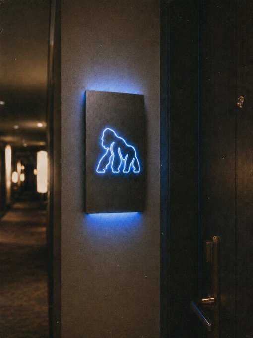 A glowing blue neon sign depicting a gorilla silhouette mounted on a dark wall in a hallway.