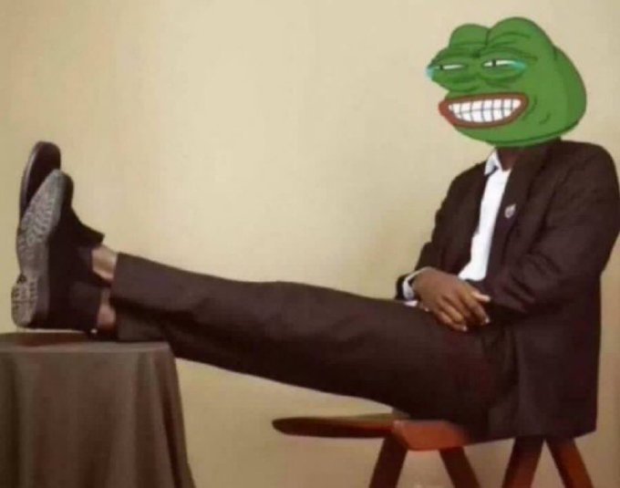 A man in a dark suit lounges with his feet propped up, his face replaced with the smug, grinning Pepe the Frog meme.