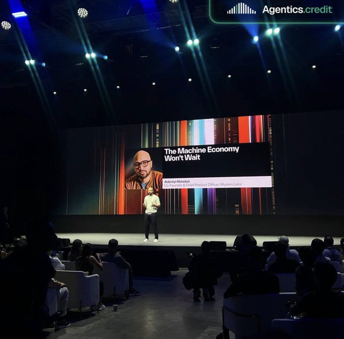 A speaker delivers a presentation titled "The Machine Economy Won't Wait" by Aidan Olincyk, Co-Founder & Chief Product Officer of Mysten Labs, at the Agentics.credit event during TOKEN2049 Singapore, connecting with major crypto industry players like Polymarket, Coinbase, and Mysten Labs to explore collaborations in agentic finance.