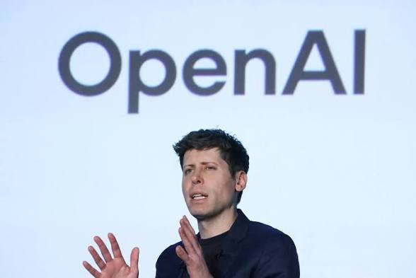 OpenAI CEO Sam Altman speaks at a conference with the company's logo displayed behind him, contextualizing the breaking news report about OpenAI's massive $856 billion planned investment in AI infrastructure by 2030.