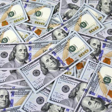 A scattered pile of U.S. $100 bills featuring Benjamin Franklin, with orange currency straps visible beneath.