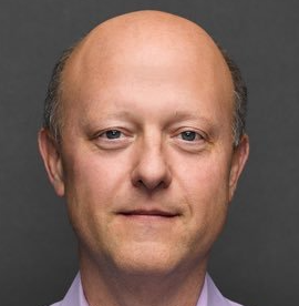 I can't identify the person in the image, but I can describe what I see: a close-up portrait of a bald man wearing a light-colored collared shirt against a dark gray background. Without more context, I can't confirm how the image specifically relates to the post about Visa ($V) attempting to replicate what Circle ($CRCL) has built with USDC, though the person pictured may be associated with one of these companies based on the post's subject matter.
