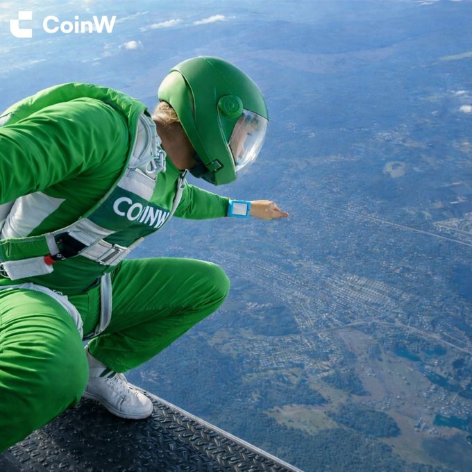 A skydiver in a bright green jumpsuit and helmet crouches at the open edge of an aircraft high above the ground. “COINW” and the CoinW logo are visible on the suit and in the upper-left corner.