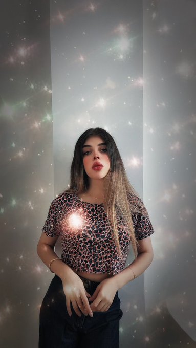 A portrait photo of a woman with long dark hair wearing a leopard print top and red lipstick, standing against a wall with a sparkly, starry light effect overlay.