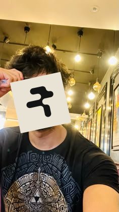 A selfie of a person with curly hair wearing a Zelda t-shirt, with a white square containing a black Devanagari 'Ra' (र) character covering their face.