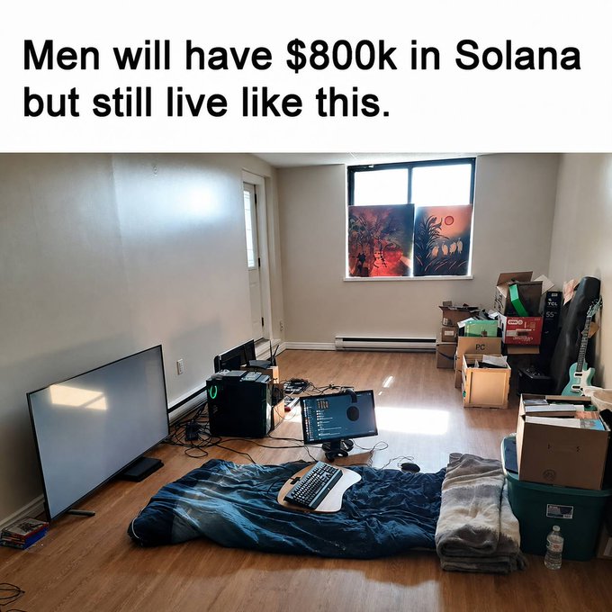 The image shows a sparse room with a sleeping bag on the floor, a TV, gaming PC setup, and scattered boxes, with the caption "Men will have $800k in Solana but still live like this." This humorously illustrates the "bed frame is just missed yield" sentiment—that crypto investors forgo basic comforts like proper furniture to maximize their investment gains.