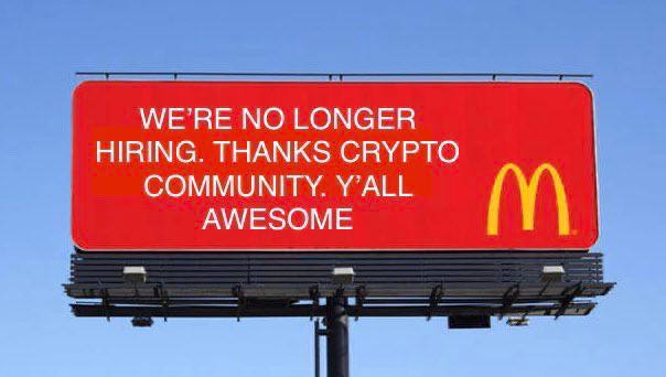 A red McDonald's billboard against a blue sky reading "WE'RE NO LONGER HIRING. THANKS CRYPTO COMMUNITY. Y'ALL AWESOME".