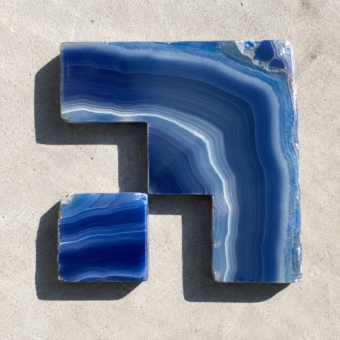 A blue and white banded agate stone carved into the shape of the number '7' or letter 'F', placed on a concrete surface.