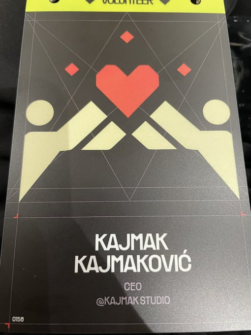 A conference badge featuring a geometric design with a red heart and two stylized figures, identifying the wearer as KAJMAK KAJMAKOVIĆ, CEO of @KAJMAK STUDIO.