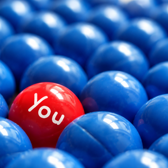 A red ball labeled 'You' stands out among a sea of identical blue balls, a common stock photo concept for individuality or standing out from the crowd.
