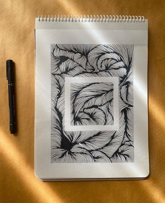 Black and white abstract ink drawing of flowing curved patterns on a spiral-bound sketchbook, with a black fineliner pen beside it on a wooden surface.