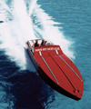 A red motorboat speeds across bright blue ocean water, leaving a white wake trailing behind it.