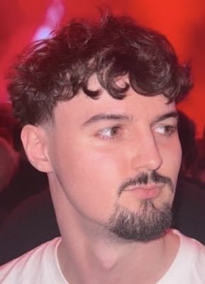 A young man with curly dark hair, a mustache, and goatee looks off to the side against a red-lit background, appearing to be at an event. The post accuses "0XETHAN" of promoting a scam token called "SCAMINU" after being labeled as a scammer on Bubblemaps.