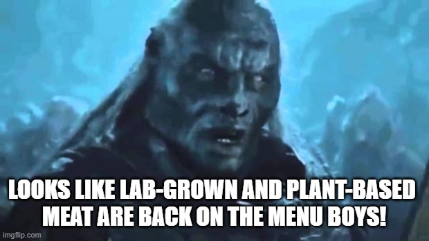 The image features a meme or cartoon style caption about lab-grown meat, which reads "looks like lab-grown and plant-based meat are back on the menu boys!". The caption also includes an image of a man with long hair wearing a black shirt, possibly representing a character from a movie.