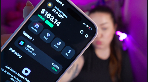 The image shows a person holding up their phone displaying a screen with information about an investment opportunity, specifically related to Bitcoin. The text on the phone reads "day 214 of buying $1 worth of SOL until ATH", which indicates that the person is monitoring the value of their Bitcoin holdings and planning to invest in it over the next few days.

The image also features a woman with long brown hair wearing a black top, who appears to be looking at her phone screen as well. The background of the image has purple lighting, adding an interesting visual element to the scene.