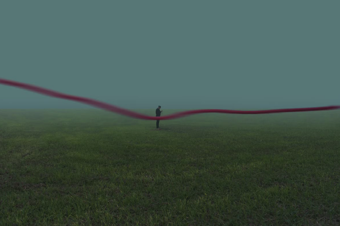 A lone figure stands in a vast, misty green field beneath a deep teal sky, holding a long flowing crimson ribbon that stretches across the frame in a gentle wave, creating a striking contrast against the muted, dreamlike landscape.