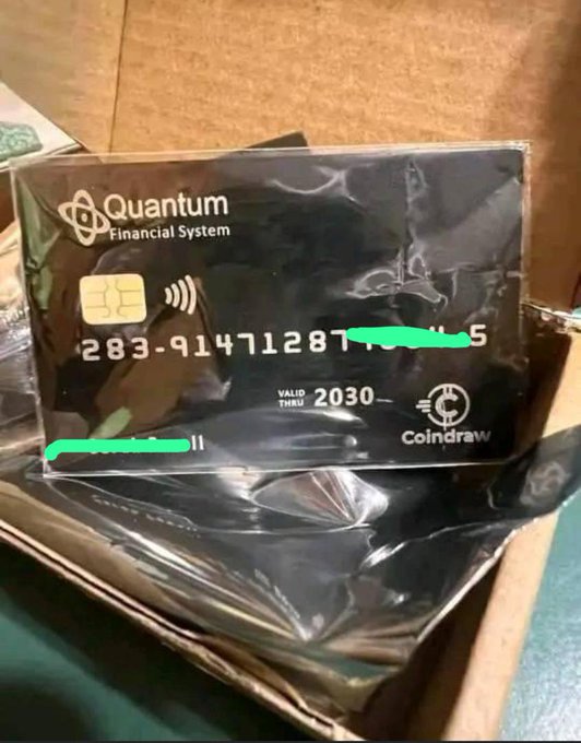 A black 'Quantum Financial System' Coindraw card with an EMV chip, valid through 2030, sealed in plastic inside a cardboard box, with the card number partially redacted in green.