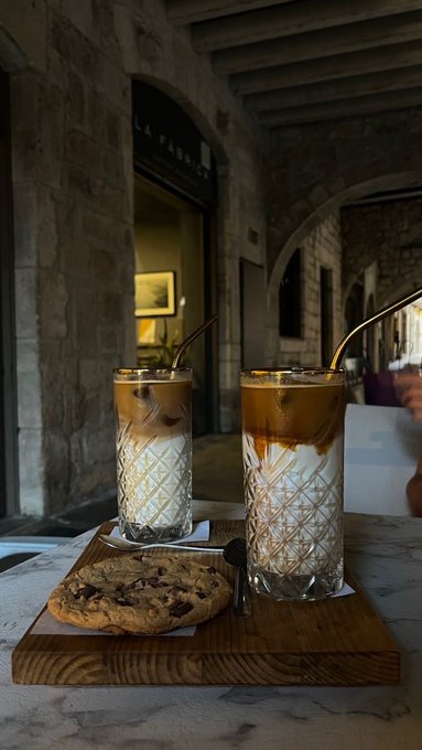 The image shows two glasses filled with coffee sitting on a wooden tray next to each other. There are also cookies placed beside the glasses, adding to the overall presentation of the scene. The background features an old stone building, which adds a touch of historical charm to the setting. The caption provided seems unrelated and does not provide any context or information about the image's content.