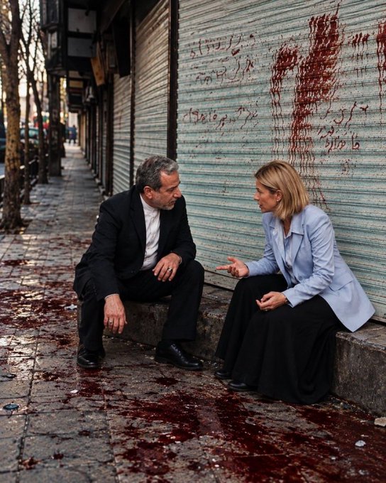 Two people in formal attire sit on a sidewalk curb having a conversation in front of a closed metal shutter with Persian text and red stains on the ground.