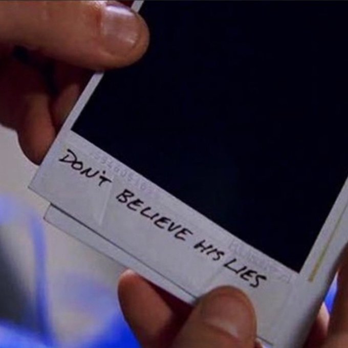 Close-up of hands holding a white smartphone with a black screen, bearing a handwritten note on tape that reads 'Don't BELIEVE HIS LIES'.