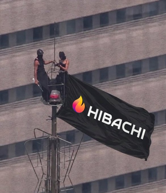 Two people on top of a tall pole structure near a building, hanging a large black flag with the 'HIBACHI' logo and flame icon.
