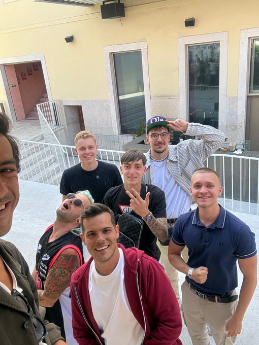 The image shows a group of six young men posing for a photo, with one man wearing a red jacket and another wearing a black shirt. The background includes a yellow building and stairs leading up to an entrance. The caption reads "this is who you are trading against part 2", which suggests that the group is participating in a challenge or competition where they have to trade off their best features for two other features, with the goal of making each other look better than before.

The image also contains text elements such as "part 1" and "part 2". These might be descriptions or instructions related to the challenge being undertaken by the group.