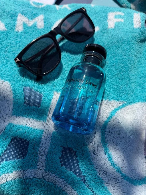 Black sunglasses and a blue bottle labeled "AFTERNOON SWIM" resting on a teal and white patterned towel.