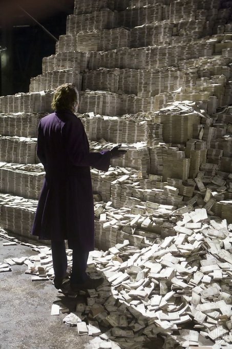 A person in a dark coat stands before an enormous wall of stacked and scattered cash bundles, echoing the "POV: you bought the right memecoin" caption by visualizing the overwhelming wealth of a successful crypto gamble. The towering piles of banded bills and loose currency spilling across the floor humorously represent the life-changing gains from picking the right viral token.
