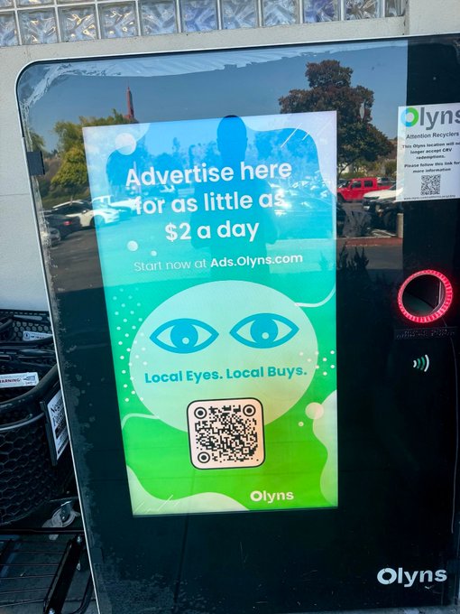An 'Olyns' advertisement on a kiosk screen promoting 'Advertise here for as little as $2 a day' with the tagline 'Local Eyes. Local Buys.'
