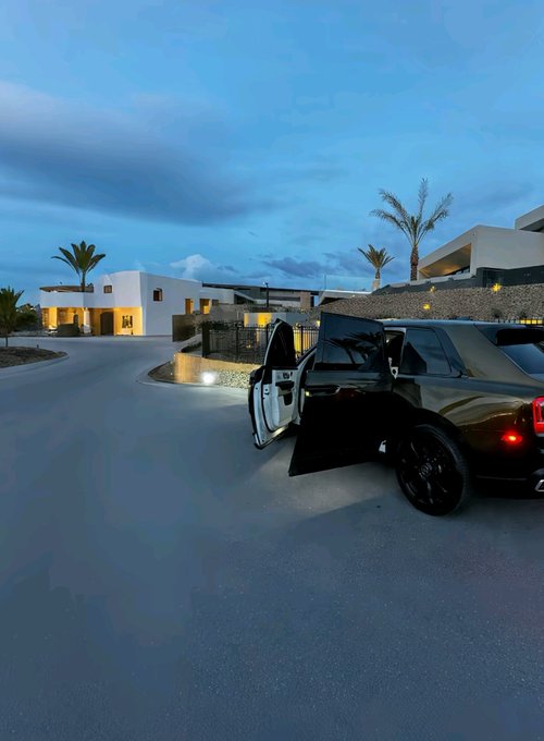 A black Rolls-Royce with its doors open sits parked on a quiet street at twilight in front of modern white villas with palm trees, evoking the luxurious lifestyle often associated with web3 success. The serene dawn setting complements the post's "Good morning web3" greeting, suggesting an aspirational morning scene.