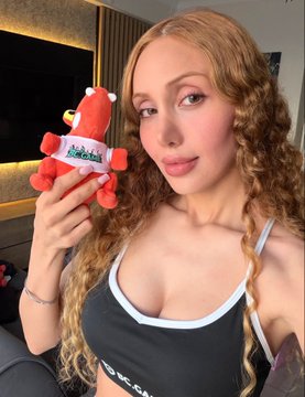 A woman with curly blonde hair holding up a small red fox plush toy with 'Nexa' written on it.