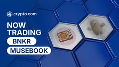 A promotional graphic from crypto.com announcing the new trading availability of $BNKR (BankrCoin) and $MUSEBOOK, displayed alongside hexagonal icons representing each token. The blue background and bold text emphasize the exchange listing news.