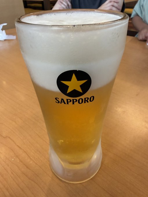 A glass of Sapporo beer with the iconic gold star logo, served on a wooden table in what appears to be a restaurant setting.