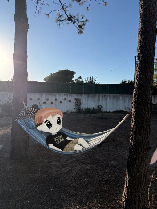 An animated cartoon figure with orange hair and a black 'Blackpink' shirt relaxes in a blue and white striped hammock strung between two pine trees in a yard at sunset.