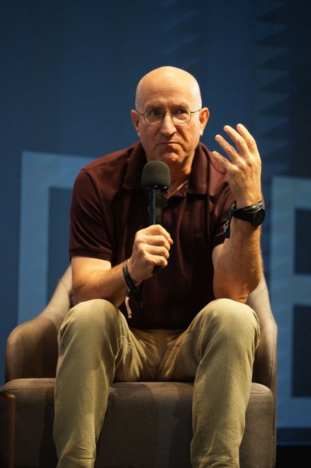 A bald man wearing glasses and a maroon polo shirt sits in a chair, holding a microphone while gesturing with his other hand during what appears to be a panel discussion or interview at an event.

The image aligns with the post's reference to Eli Ben Sasson of StarkWare speaking at the Longitude event about Bitcoin's challenges in preparing for quantum computing and the need for a soft fork to address security concerns.