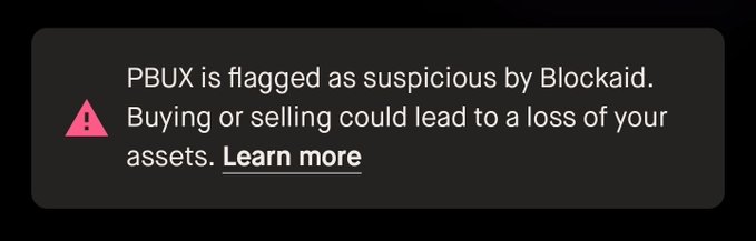 A dark-themed warning banner stating 'PBUX is flagged as suspicious by Blockaid. Buying or selling could lead to a loss of your assets.' with a 'Learn more' link.