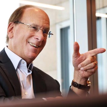 Larry Fink, CEO of BlackRock, smiling and gesturing during what appears to be an interview or speaking engagement, visually representing the financial giant behind the $136.5 million Bitcoin acquisition mentioned. The image reinforces the post's message about institutional involvement in cryptocurrency, with Fink's confident demeanor symbolizing the corporate power quietly accumulating Bitcoin while retail investors watch price movements.